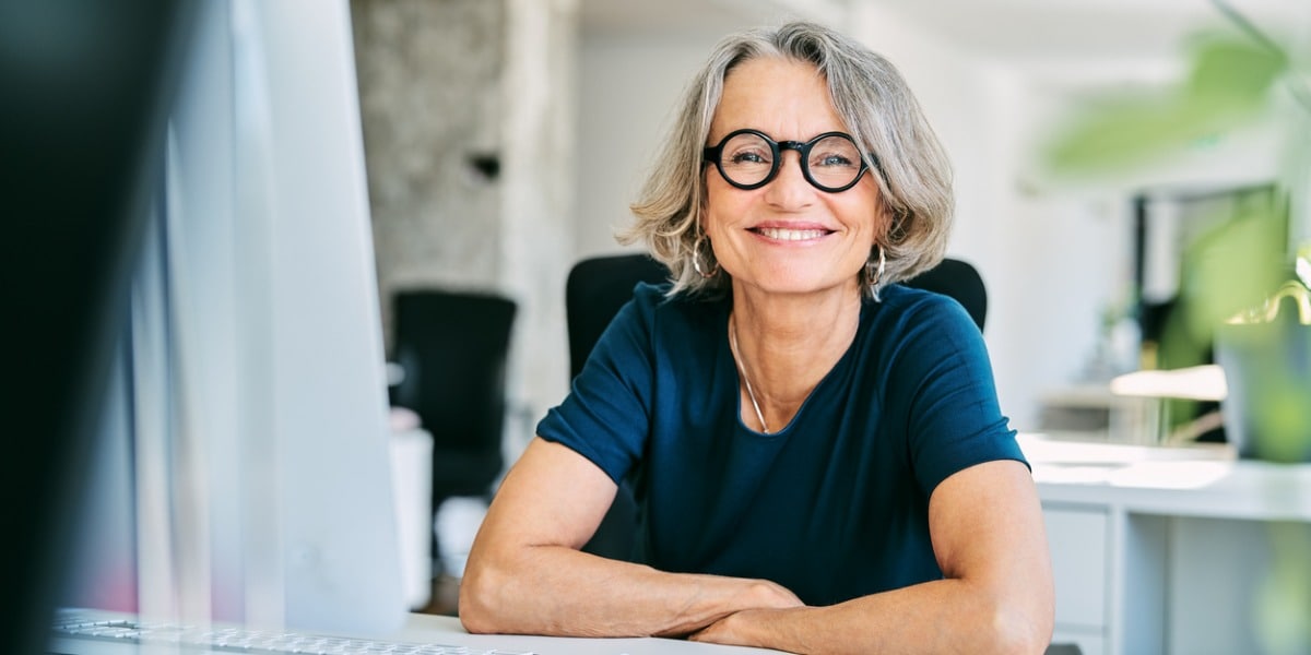 Smiling woman sitting with her arms crossed at a desk in an office