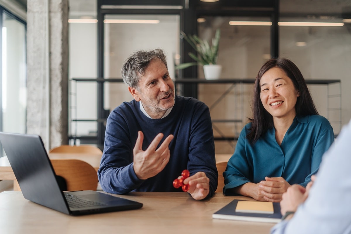Man and lady sitting at large office table with laptop 